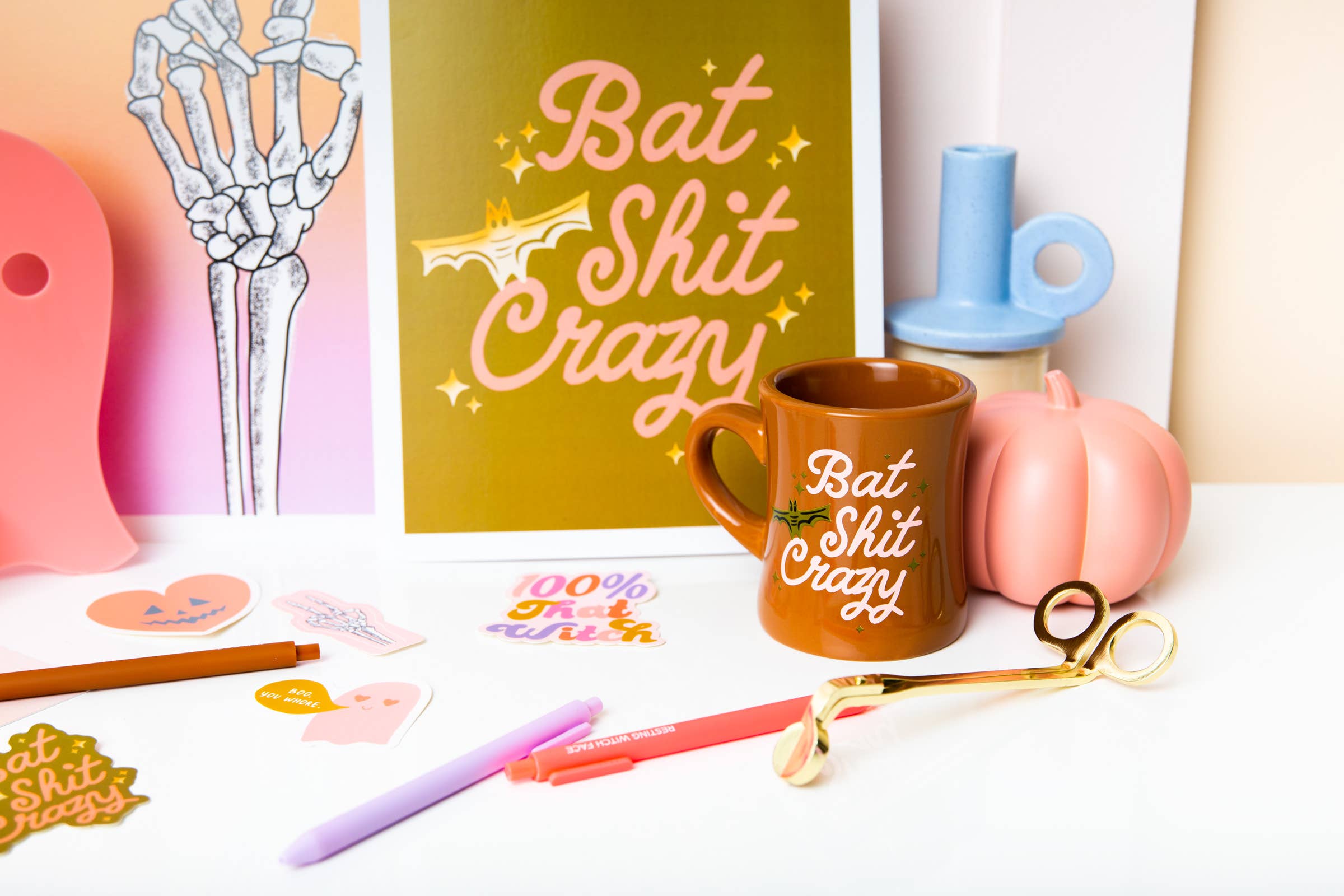cute Mug with 'Bat Shit Crazy' text on a table with stationery items and a decorative sign.