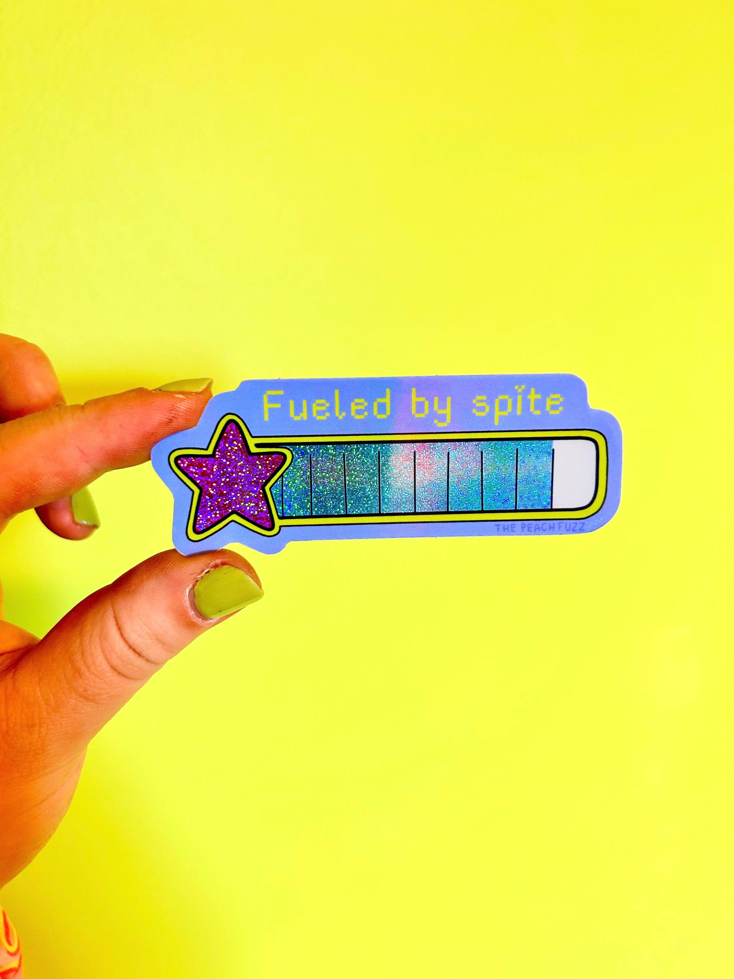 Sticker with 'Fueled by spite' text held against a yellow background