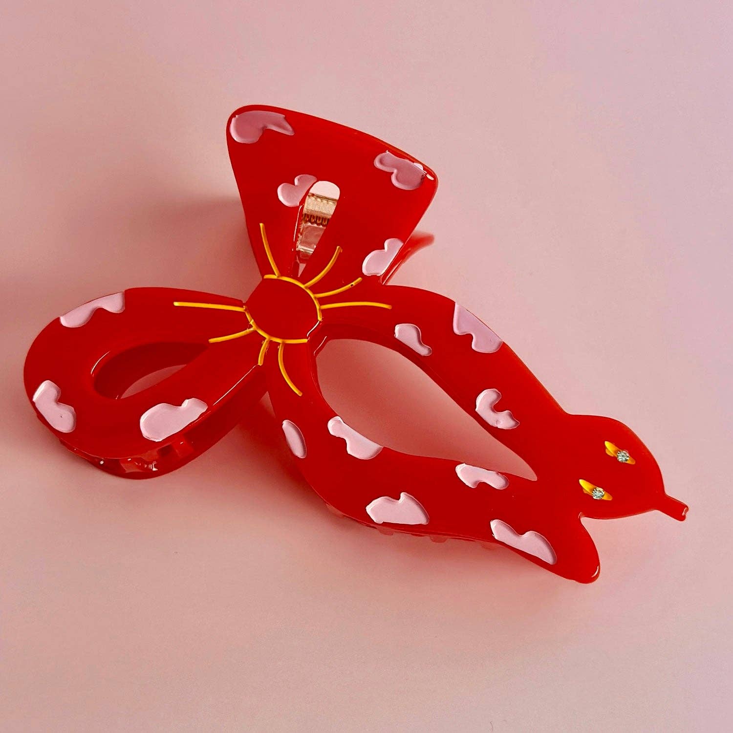 Red bow-shaped hair clip that's a snake with white polka dot hearts on a pink background