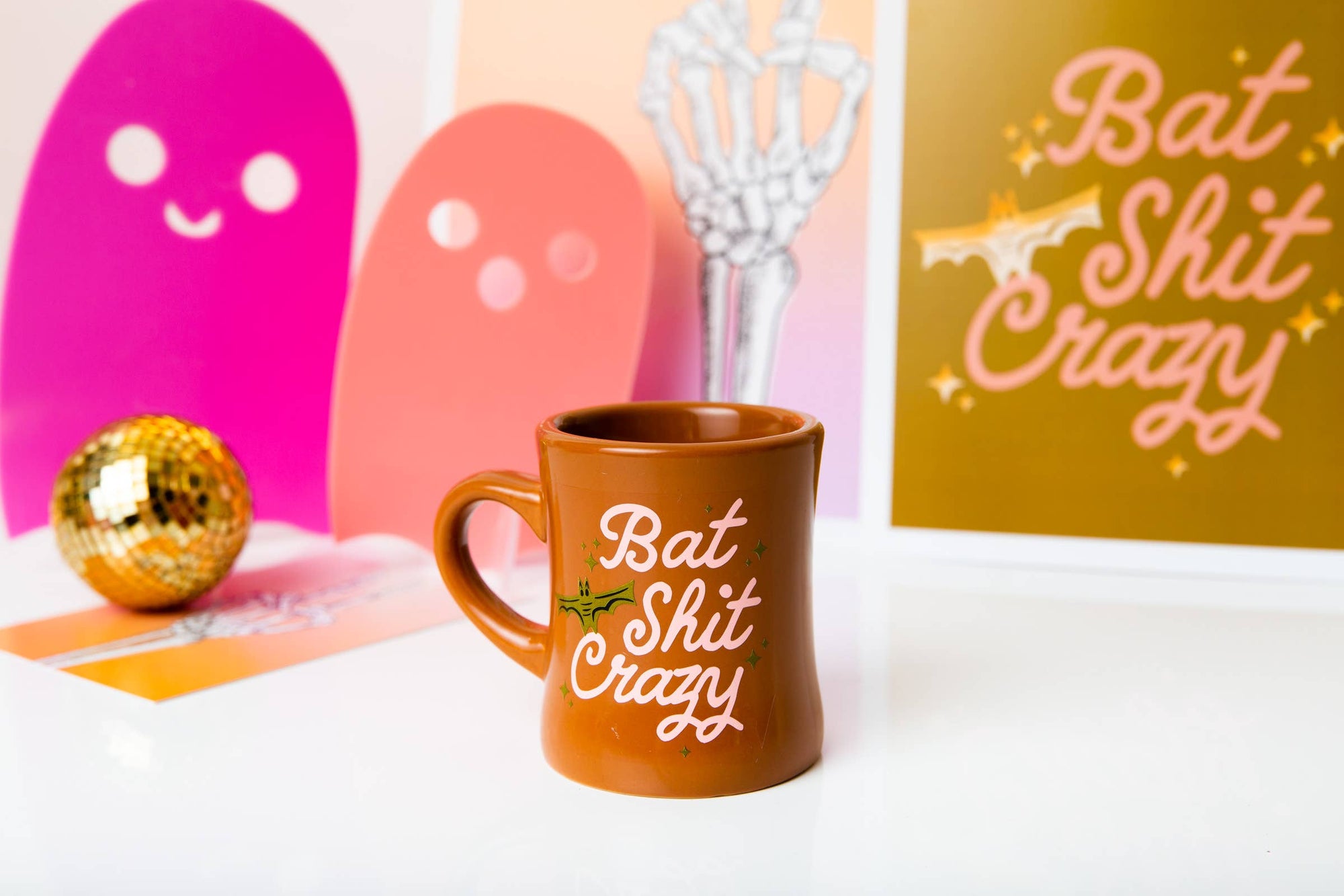 Brown mug with 'Bat Shit Crazy' text on a white surface with colorful background