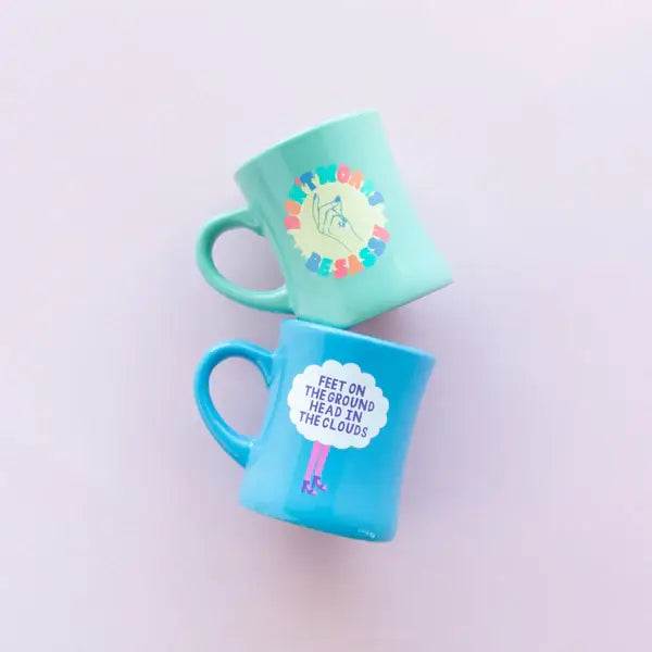Two mugs, one green and one blue, with colorful designs on a light purple background.