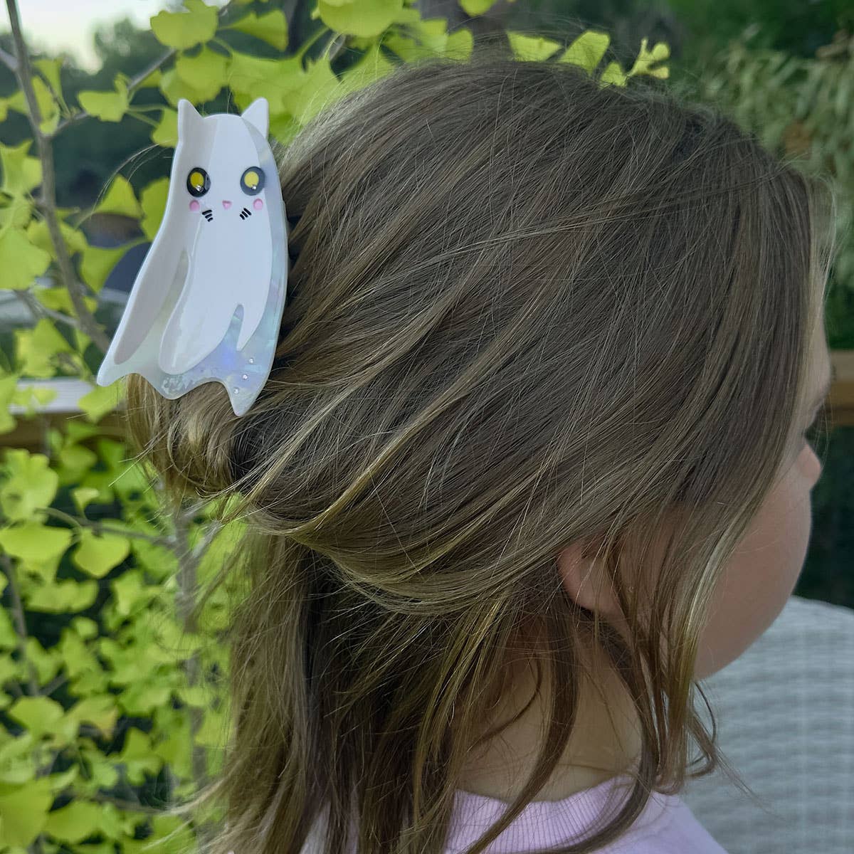 Child with a ghost-shaped cat hair clip in their hair, outdoors.