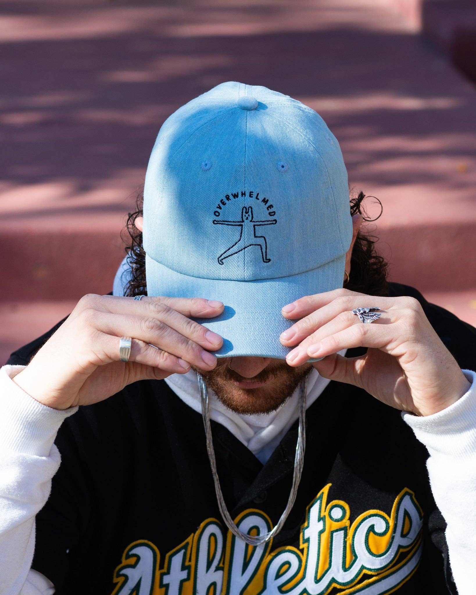 Person wearing a light blue cap with an overwhelmed yoga pose design against a brick stair background