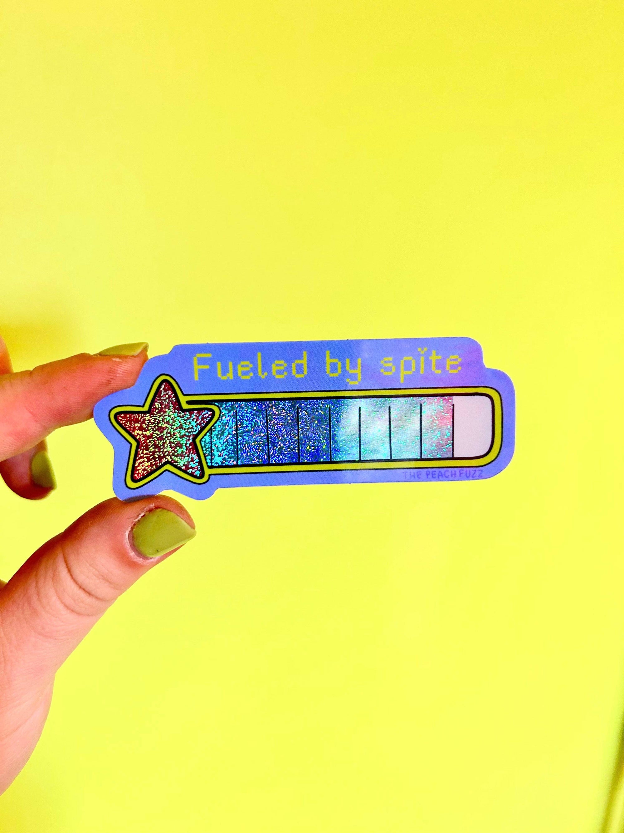 Sticker with star design and text 'Fueled by spite' held against a yellow background