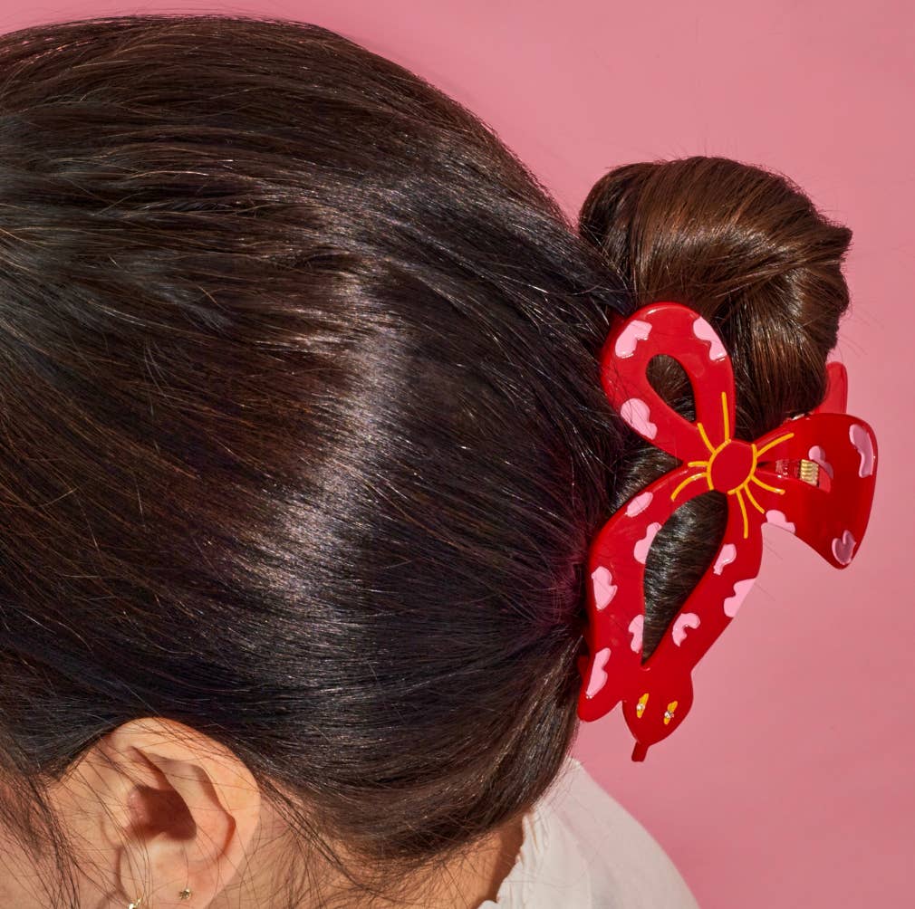Red hair ribbon snake clip with a bow design in a brunette's hair on a pink background