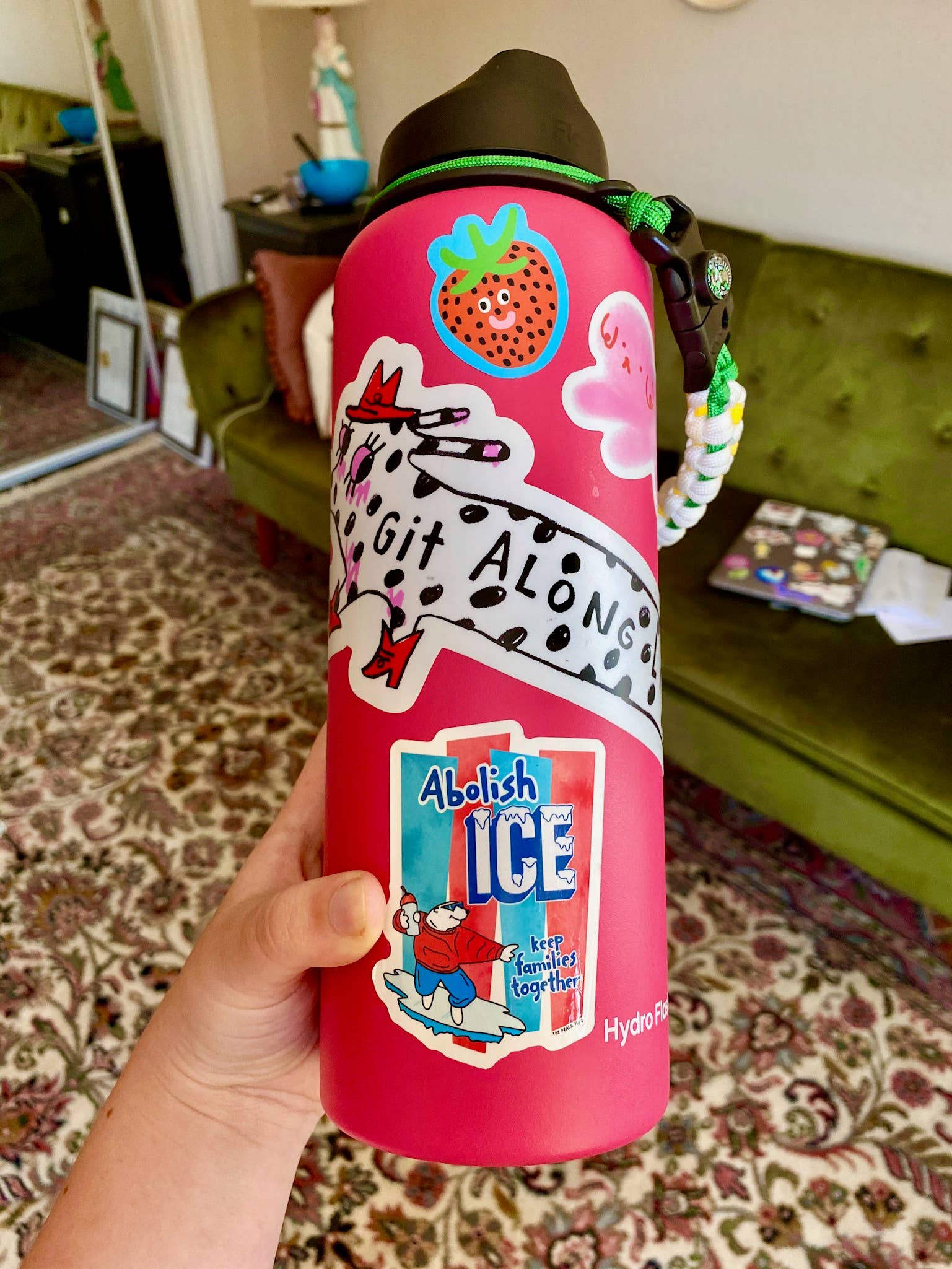 Pink water bottle with cartoon designs held in a hand, with a room interior in the background.