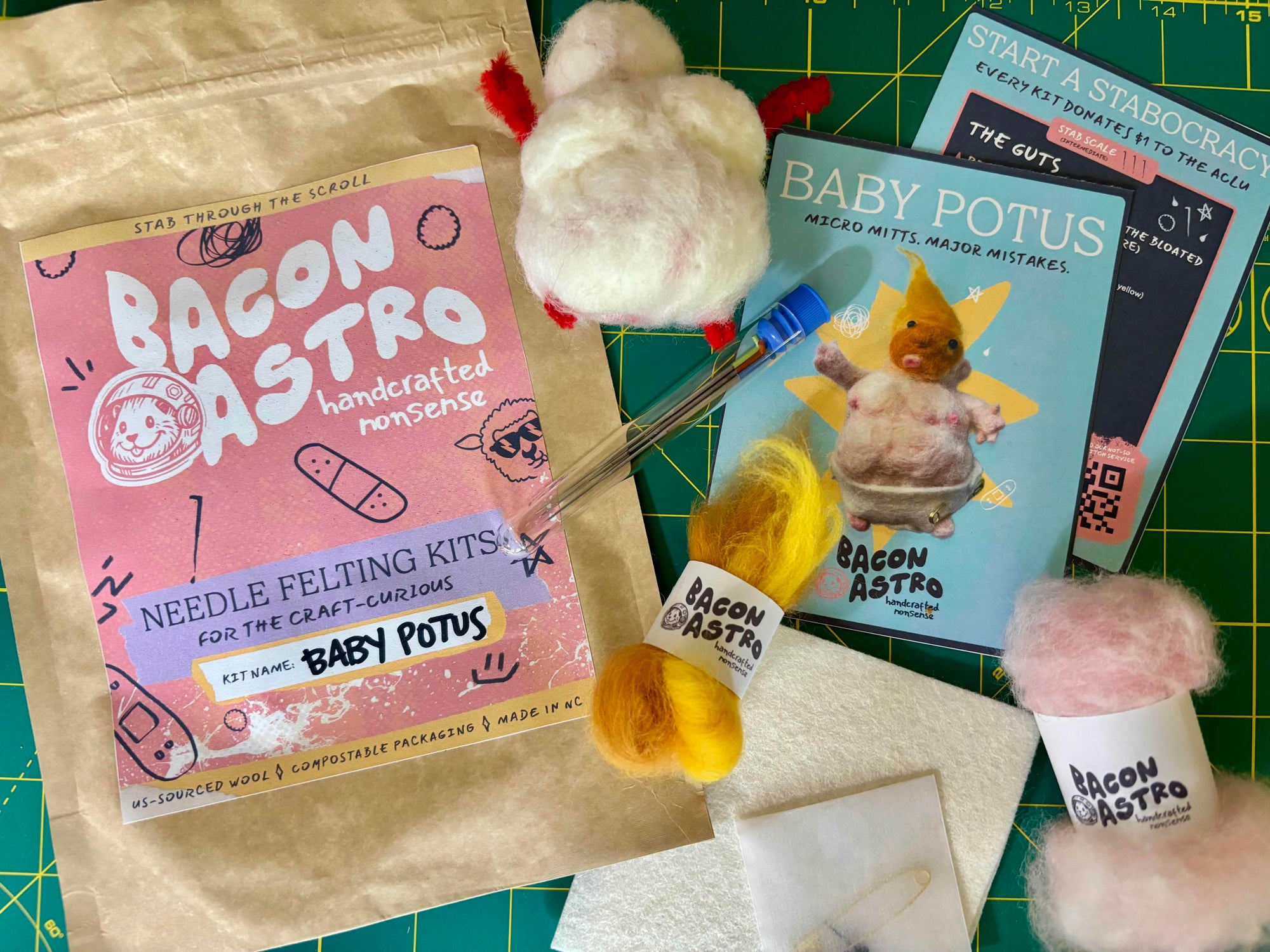 Bacon Astro needle felting kit with wool, needles, armature, felt fabric, and packaging on a green cutting mat