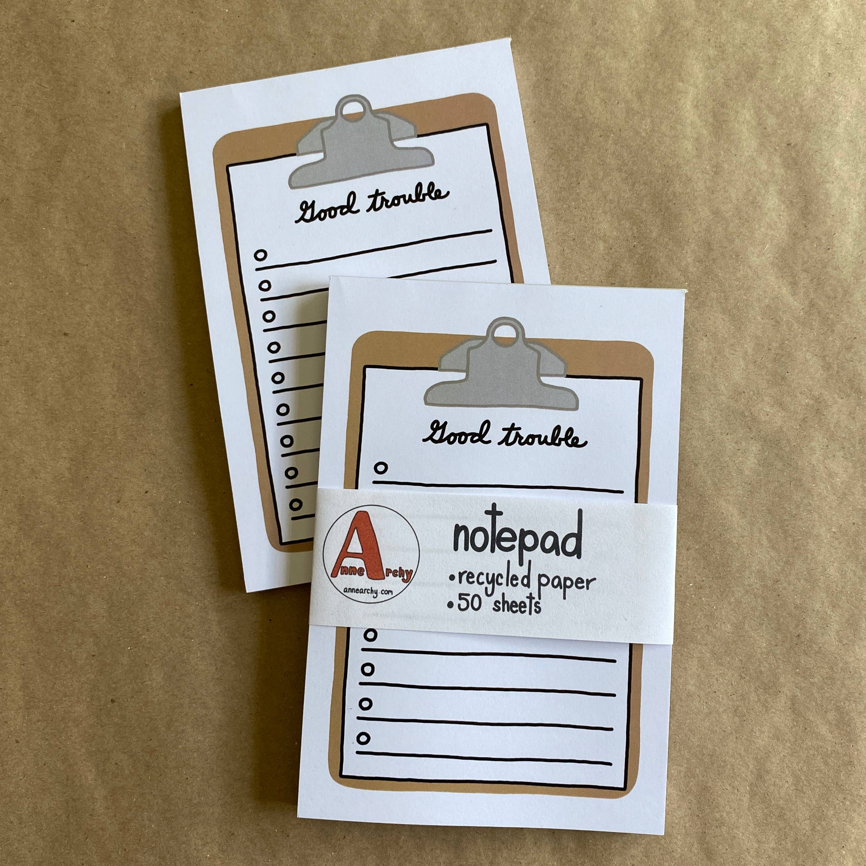 Two small notepads with a clip on top, labeled 'Good trouble', on a brown background.
