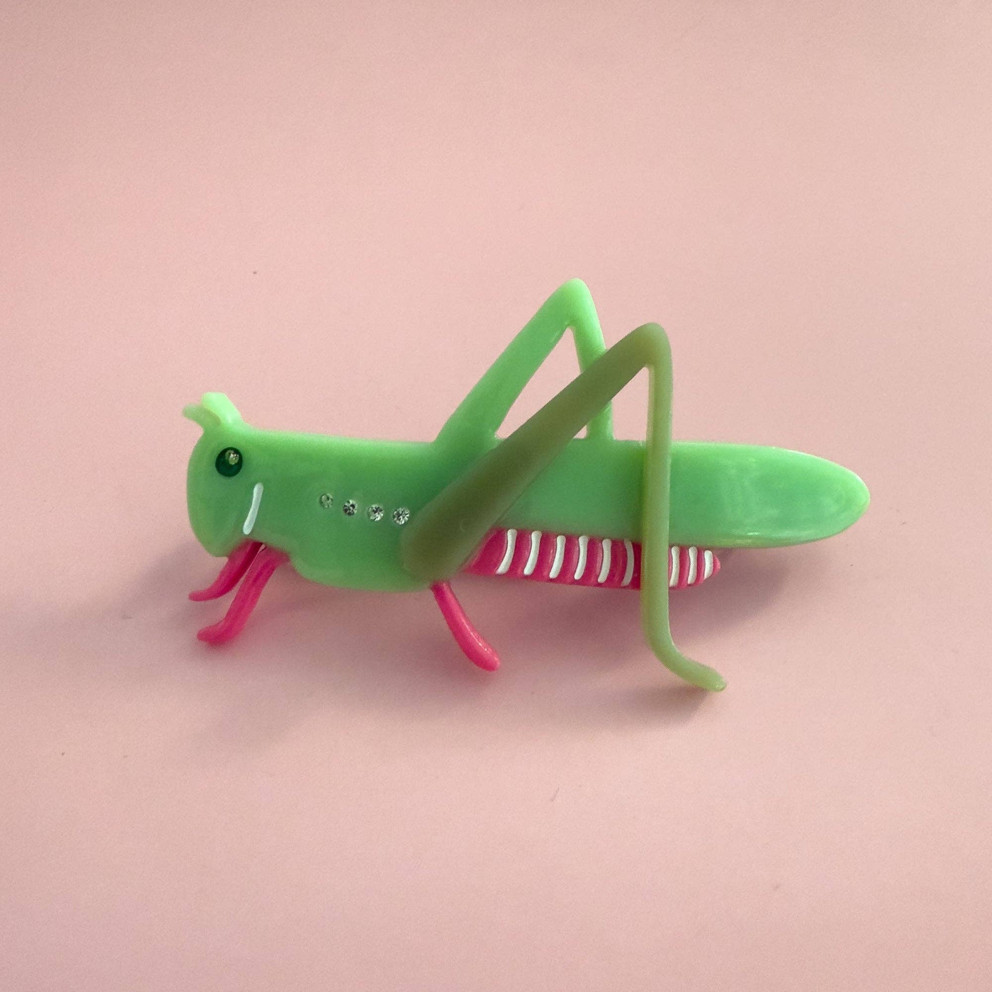 Green grasshopper hair claw with pink legs on a pink background