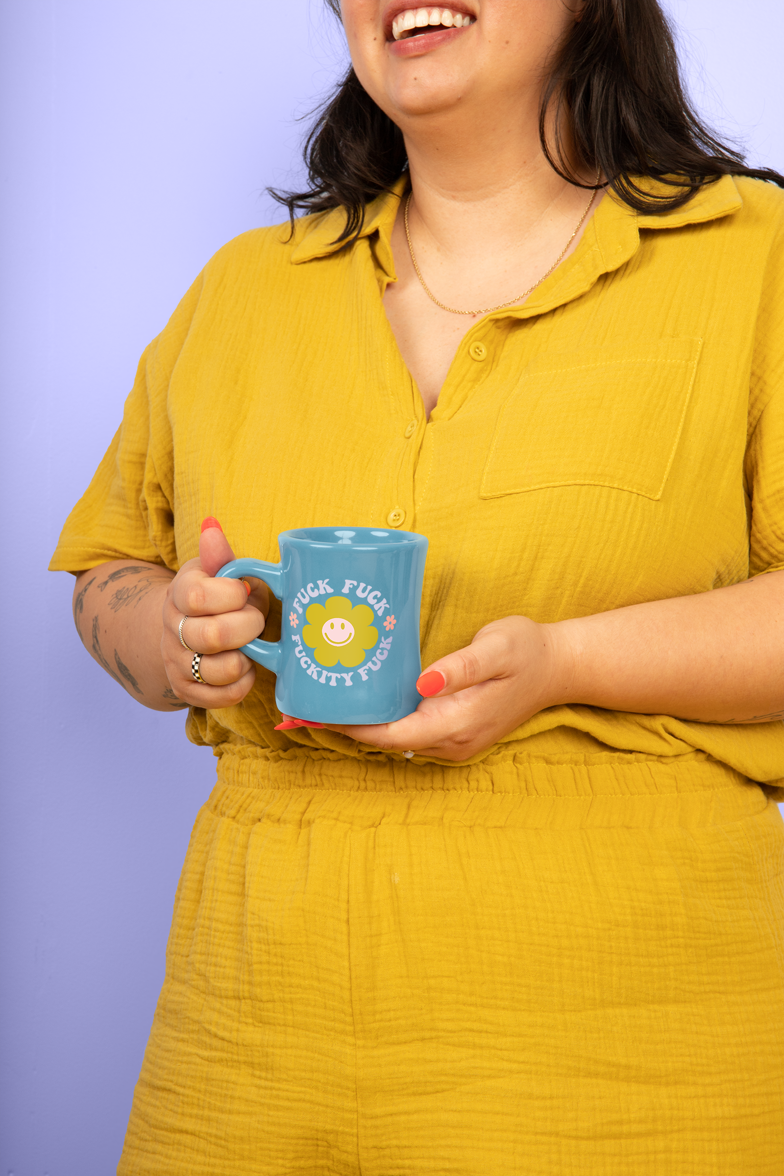 Person wearing a yellow outfit holding a blue mug with a sassy yellow flower graphic design against a purple background