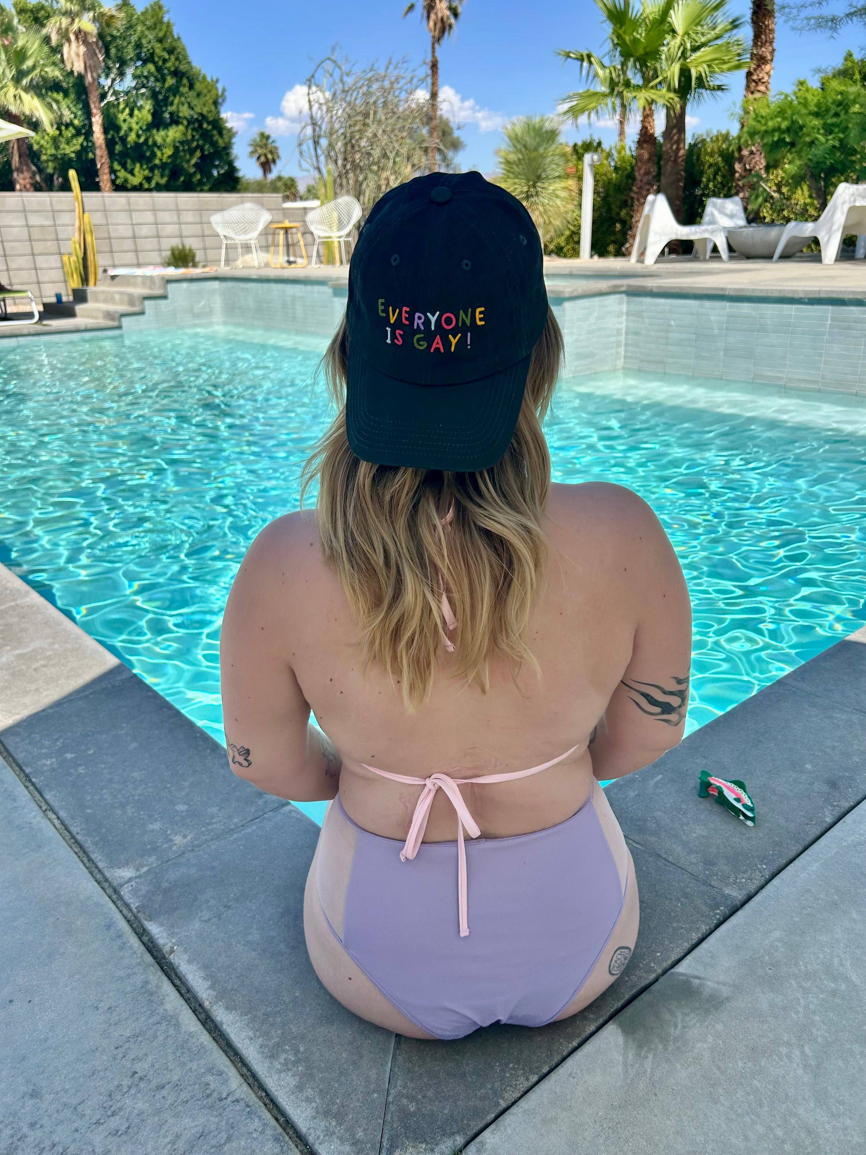 Person wearing a 'Everyone is Gay!' cap by a pool