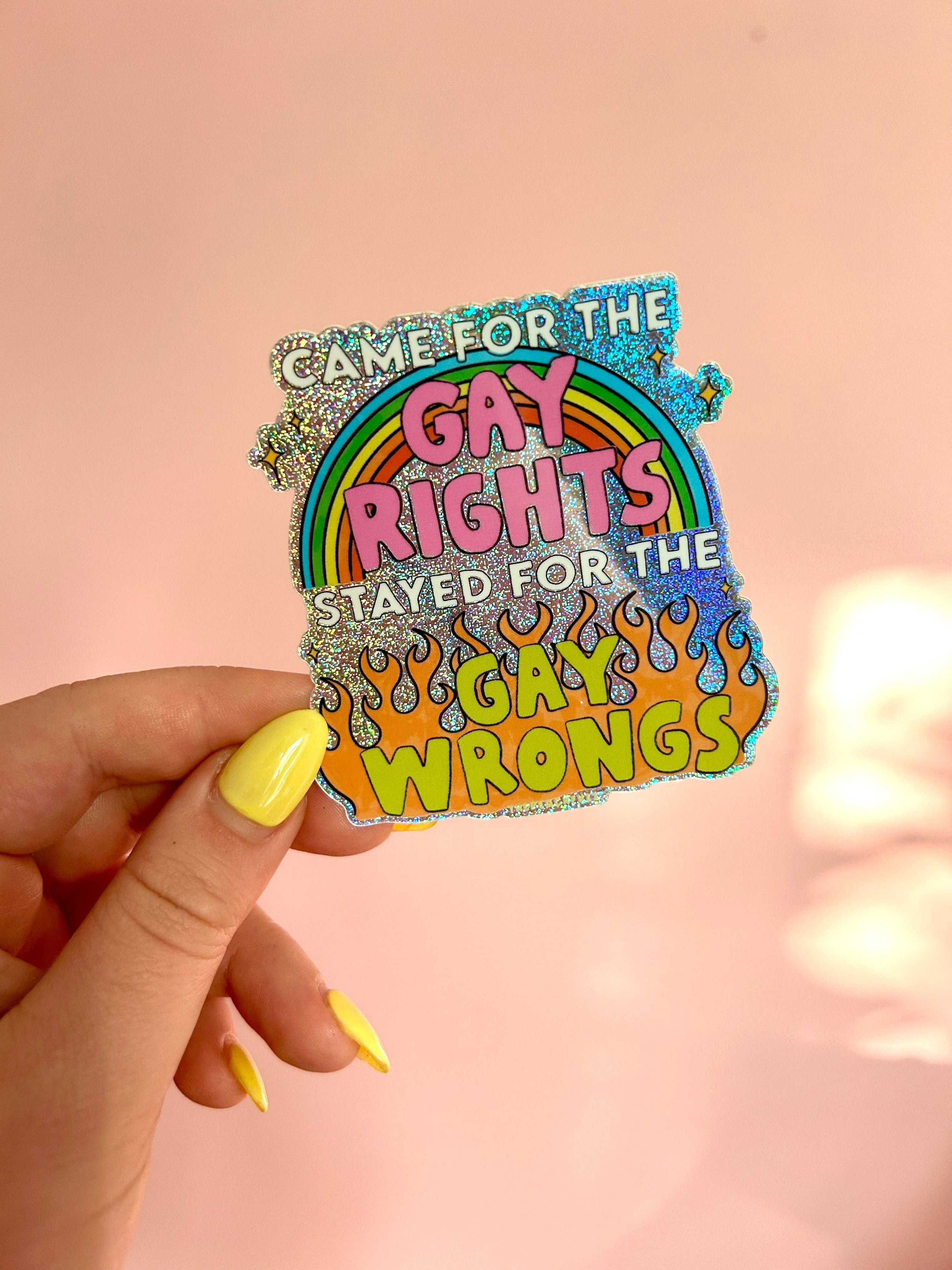 Sticker with rainbow design and text held by a hand against a pink background