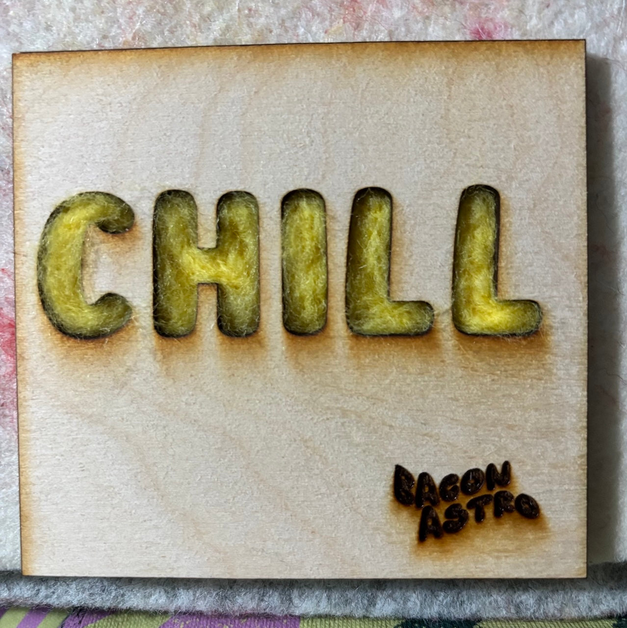 Wooden stencil with 'CHILL' text and 'BaconAstro' branding on a textured surface.
