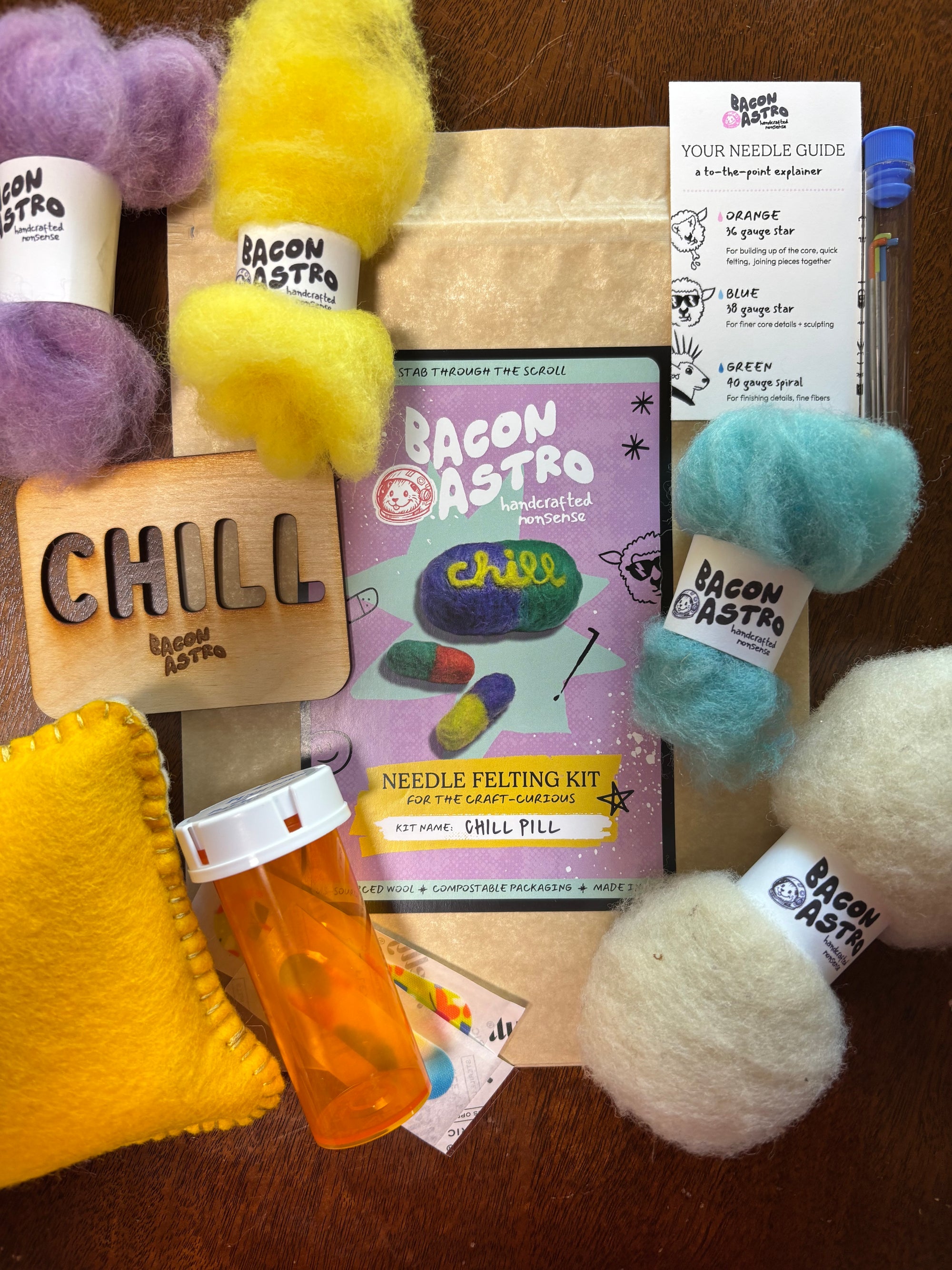 Bacon Astro needle felting kit with colorful wool and felted items on a wooden surface.