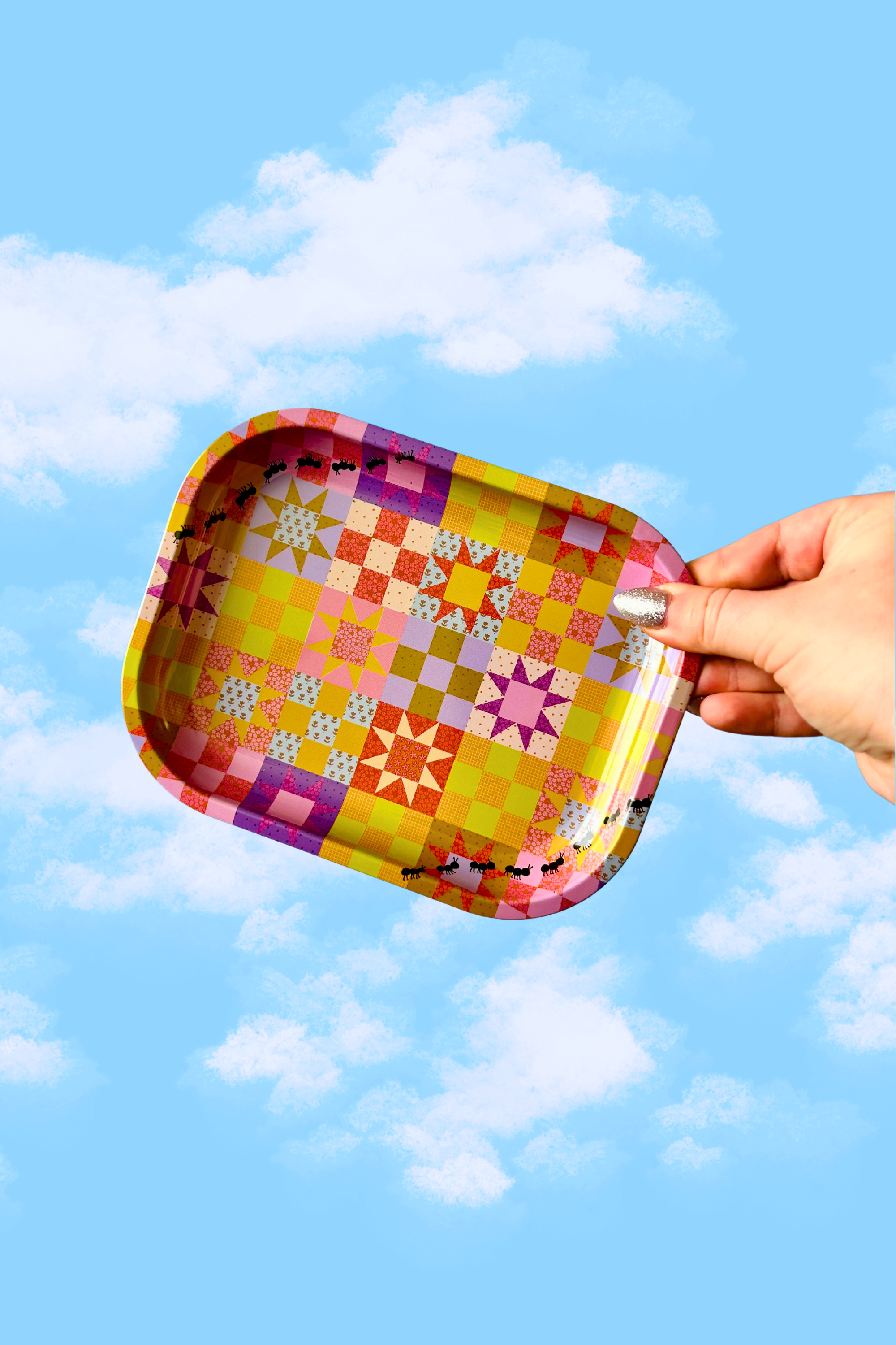 Hand holding a colorful quilt patterned tray against a blue sky with clouds - sewing crafters