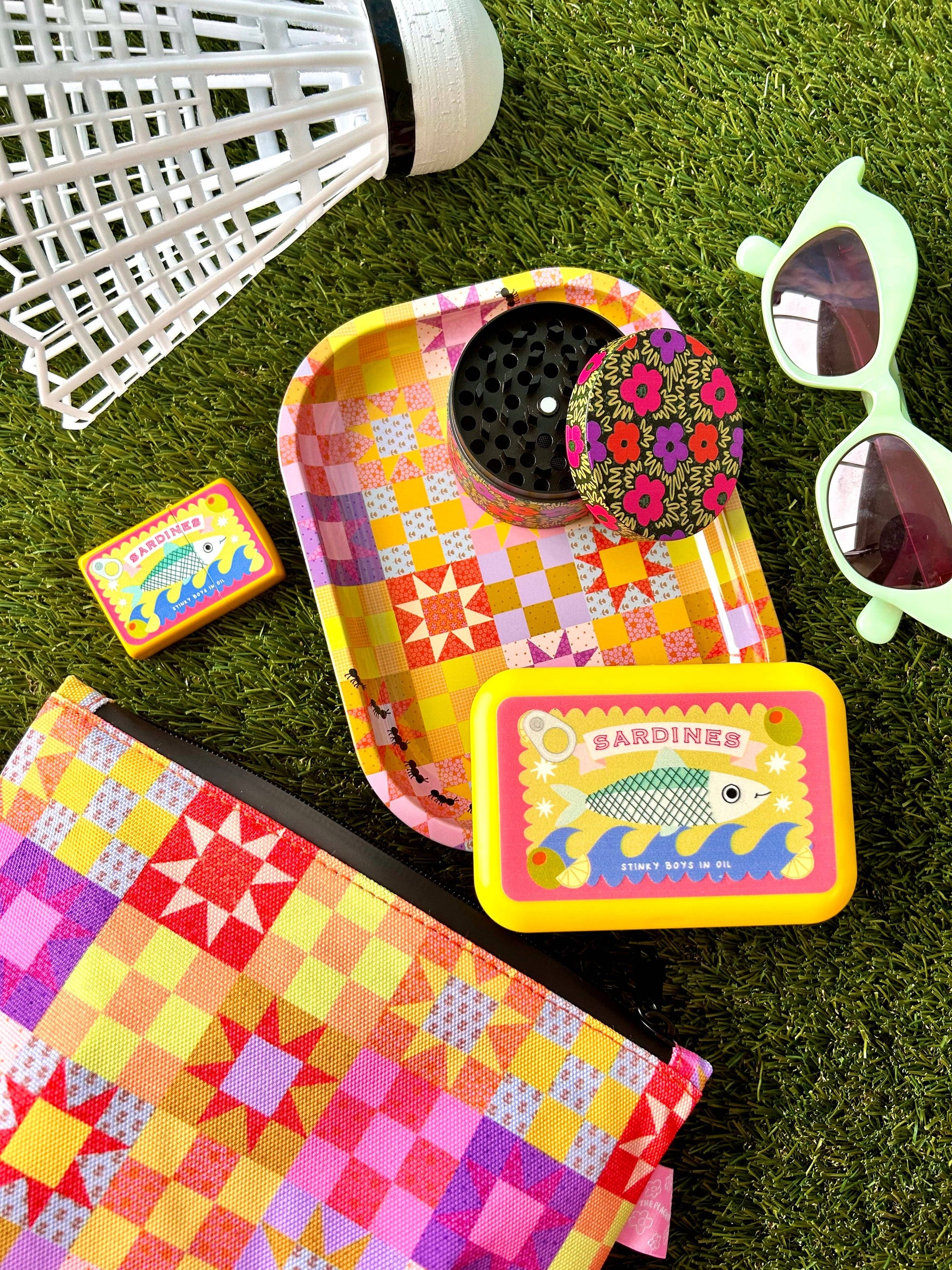 Colorful quilt tray with floral lid, sunglasses, and snack packaging on grass