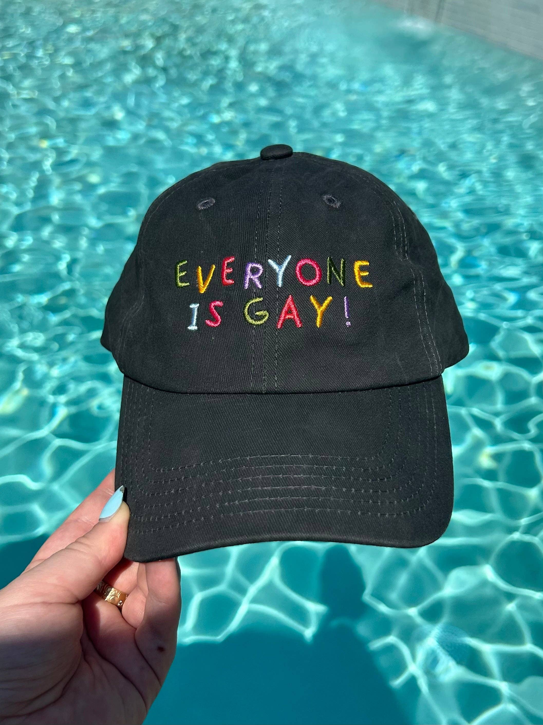 Black cap with 'EVERYONE IS GAY!' text held over a pool