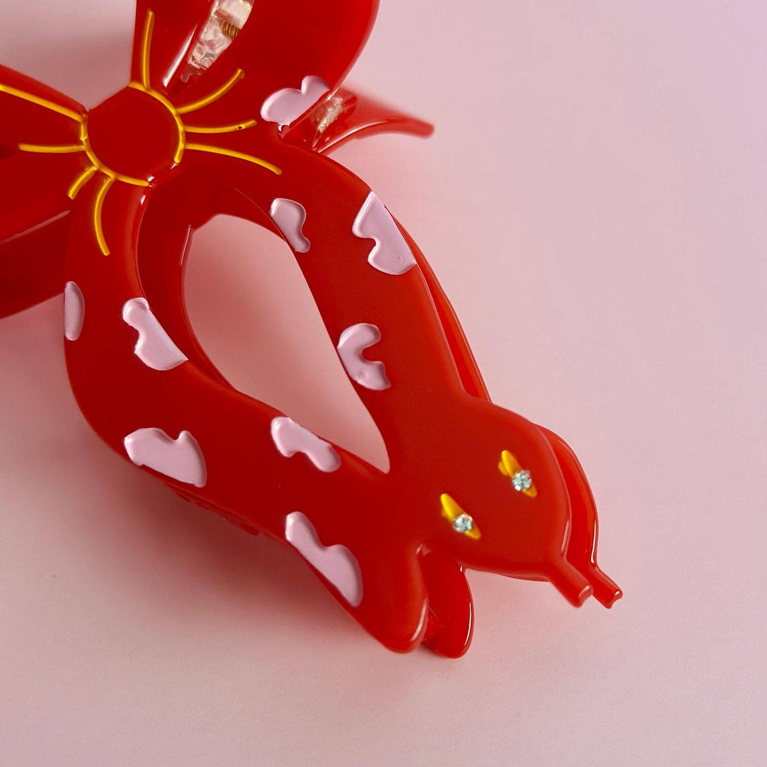 Red snake-shaped hair clip with yellow accents on a pink background
