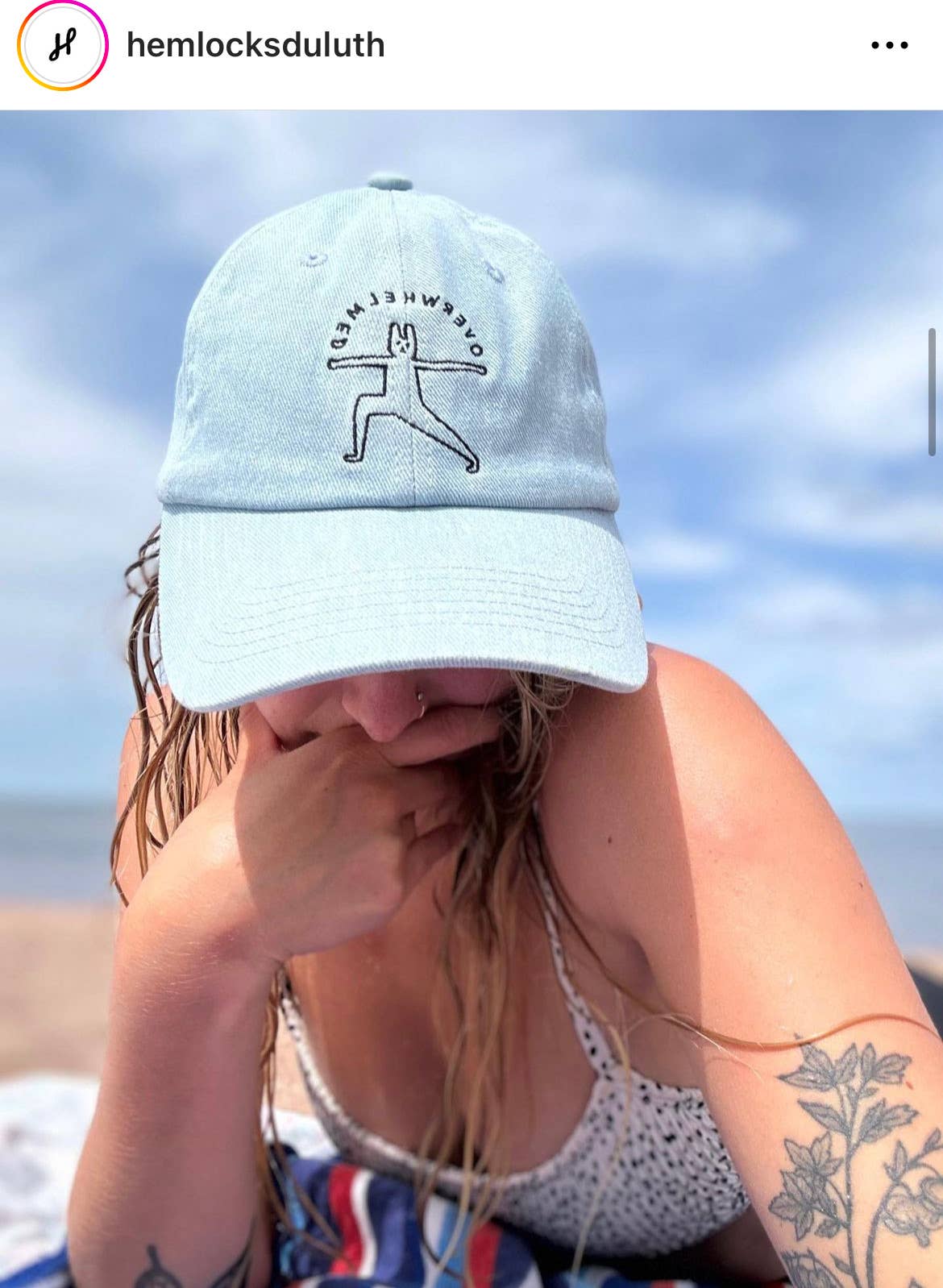 Person wearing a light blue cap with a logo, sitting on a beach.