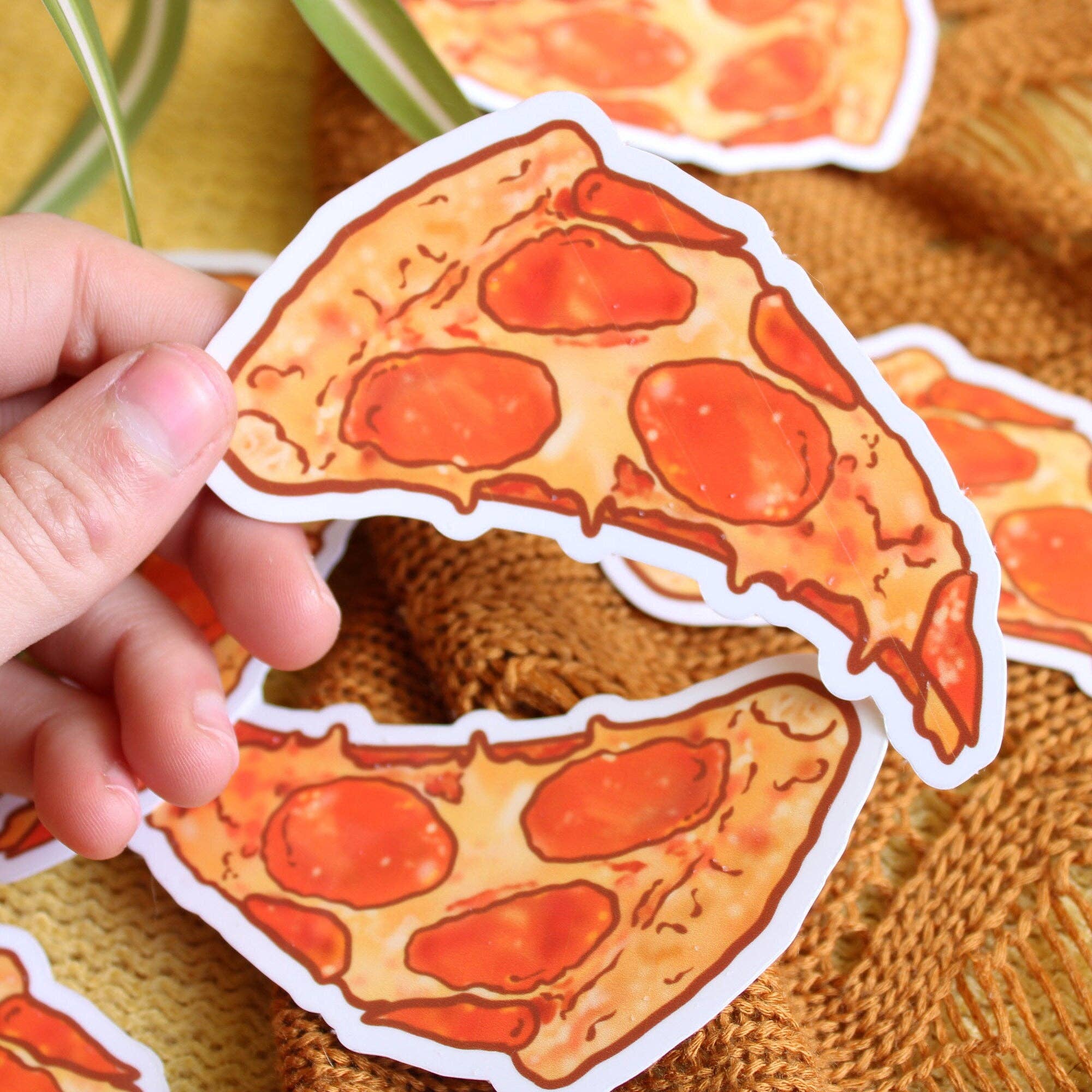 Hand holding a pepperoni pizza slice sticker on a textured surface