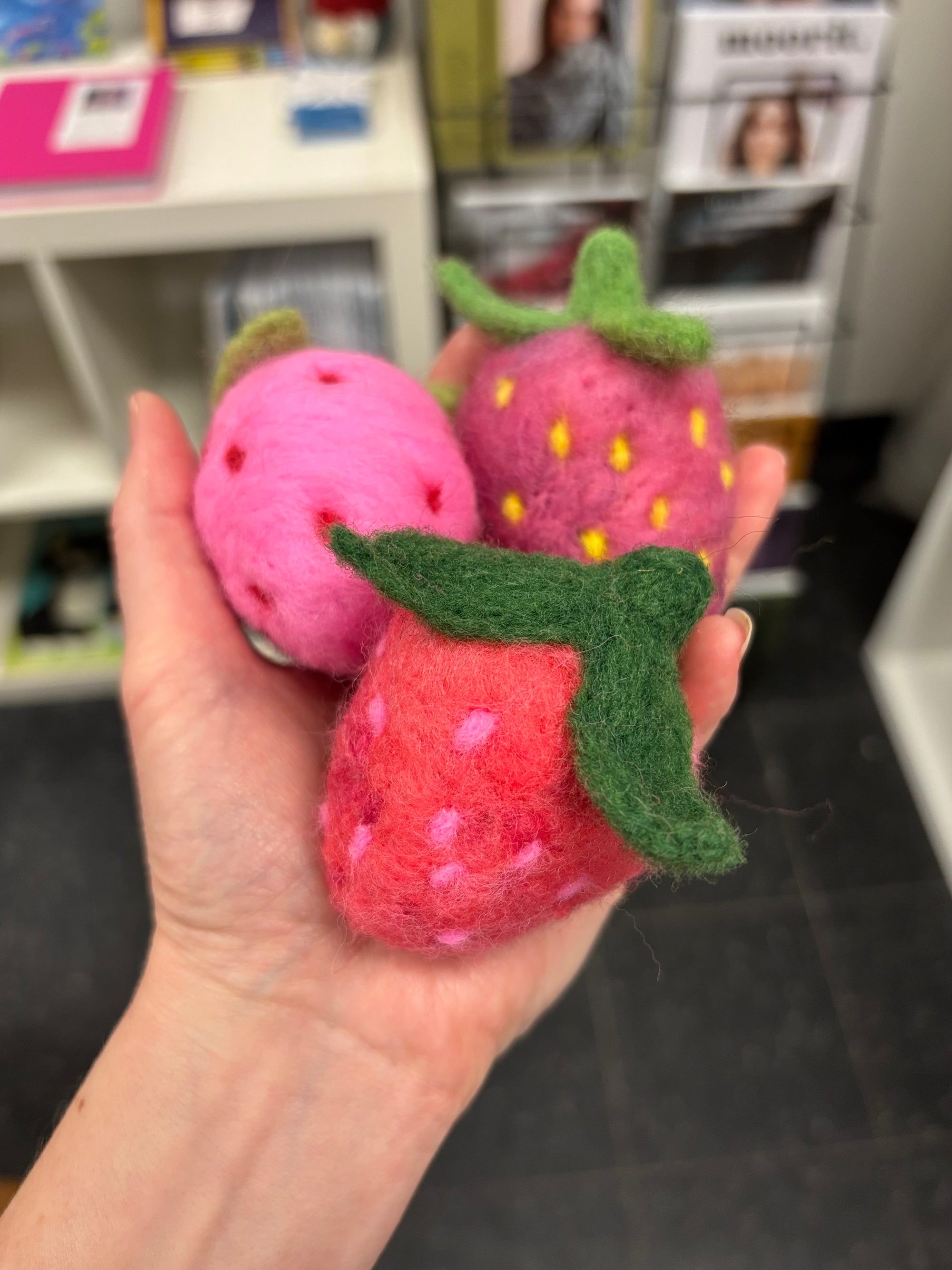 a hand holding pink and red fuzzy strawberry pin cushion - 100 percent wool handmade from needlefelting