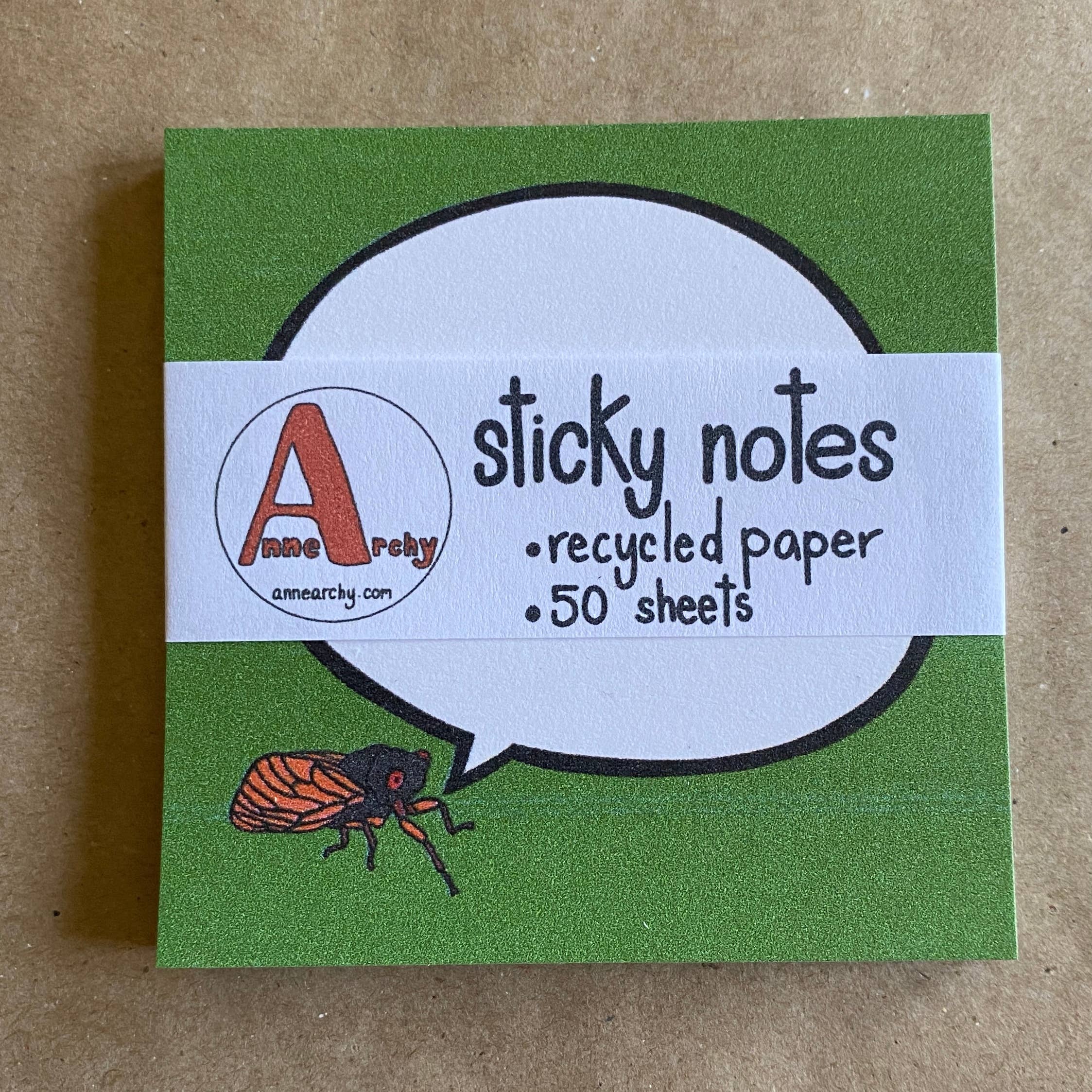 Box of green recycled paper sticky notes with a cicada illustration on a brown background