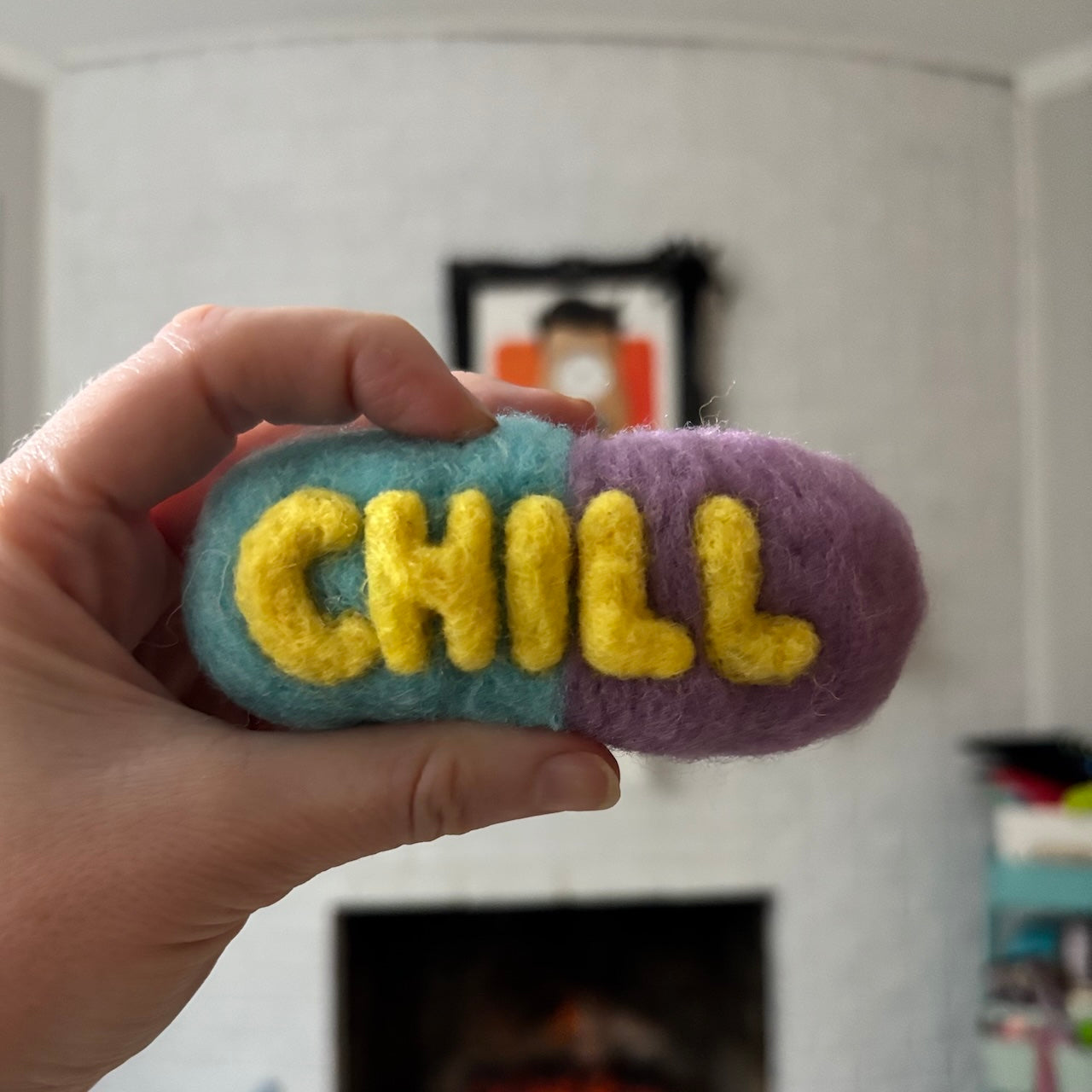 Hand holding a colorful plush toy with 'CHILL' text against a blurred indoor background
