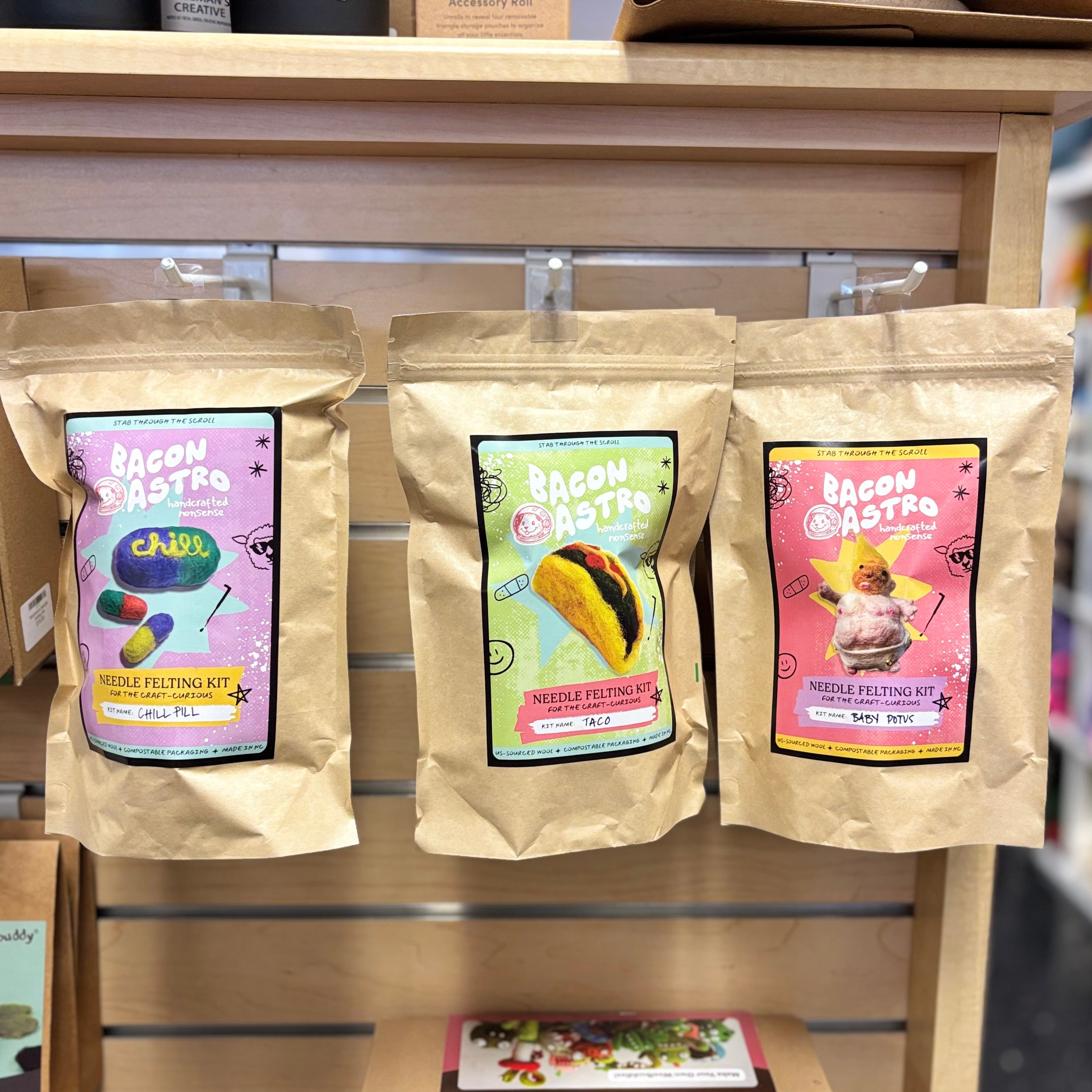 Three needle felting kit packages on a wooden shelf