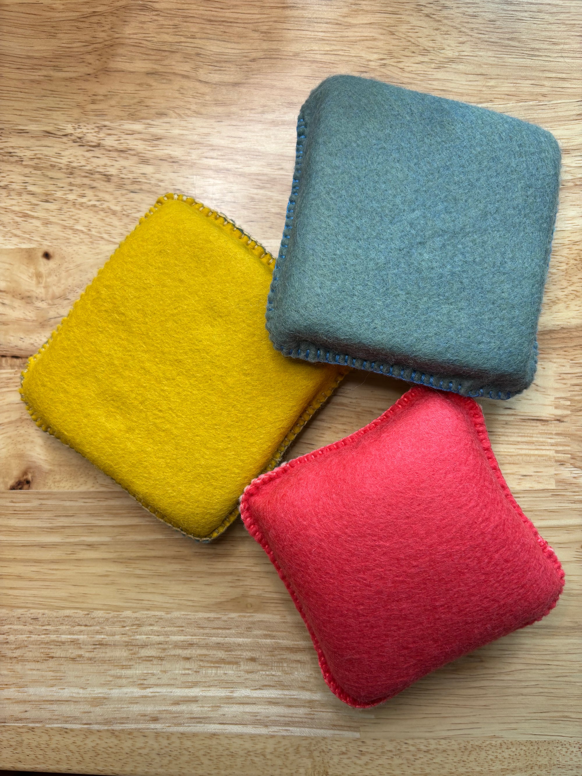 Three colorful square needle felting mats  (yellow, blue, red) on a wooden surface